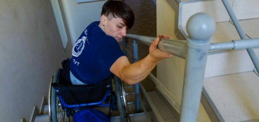 A determined individual in a wheelchair on stairs, using a handrail for support.