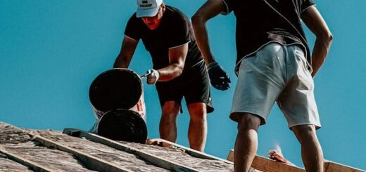 Two construction workers apply roofing materials under a bright blue sky, showcasing teamwork and labor.
